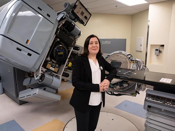 Person standing in a medical treatment room with advanced radiotherapy equipment, including a large Varian machine and treatment table.