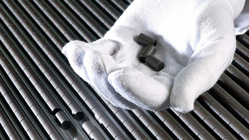 A white gloved hand holds 3 nuclear pellets with rows of nuclear pellets in the background