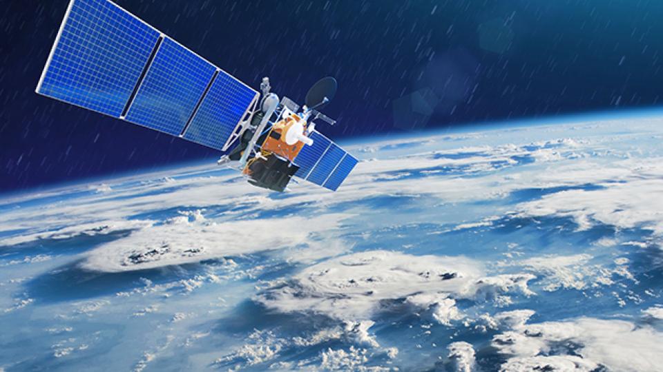 Satellite with large blue solar panels orbiting above Earth, showing cloud formations and the planet&#039;s curvature against a dark space background